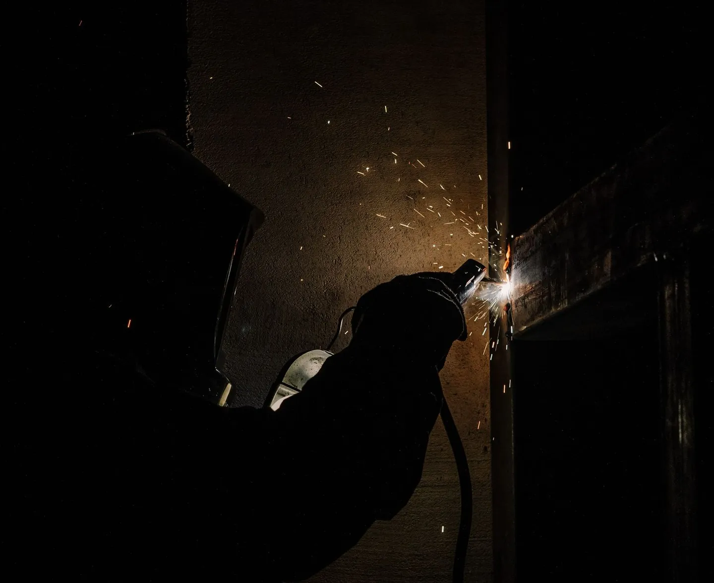 Soldador trabajando en un taller oscuro, con chispas